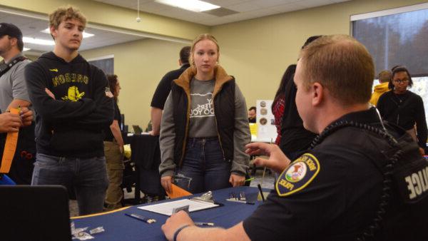 Two students chat with a uniformed man at a table.