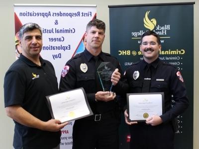 3 people with certificates & awards in front of banners